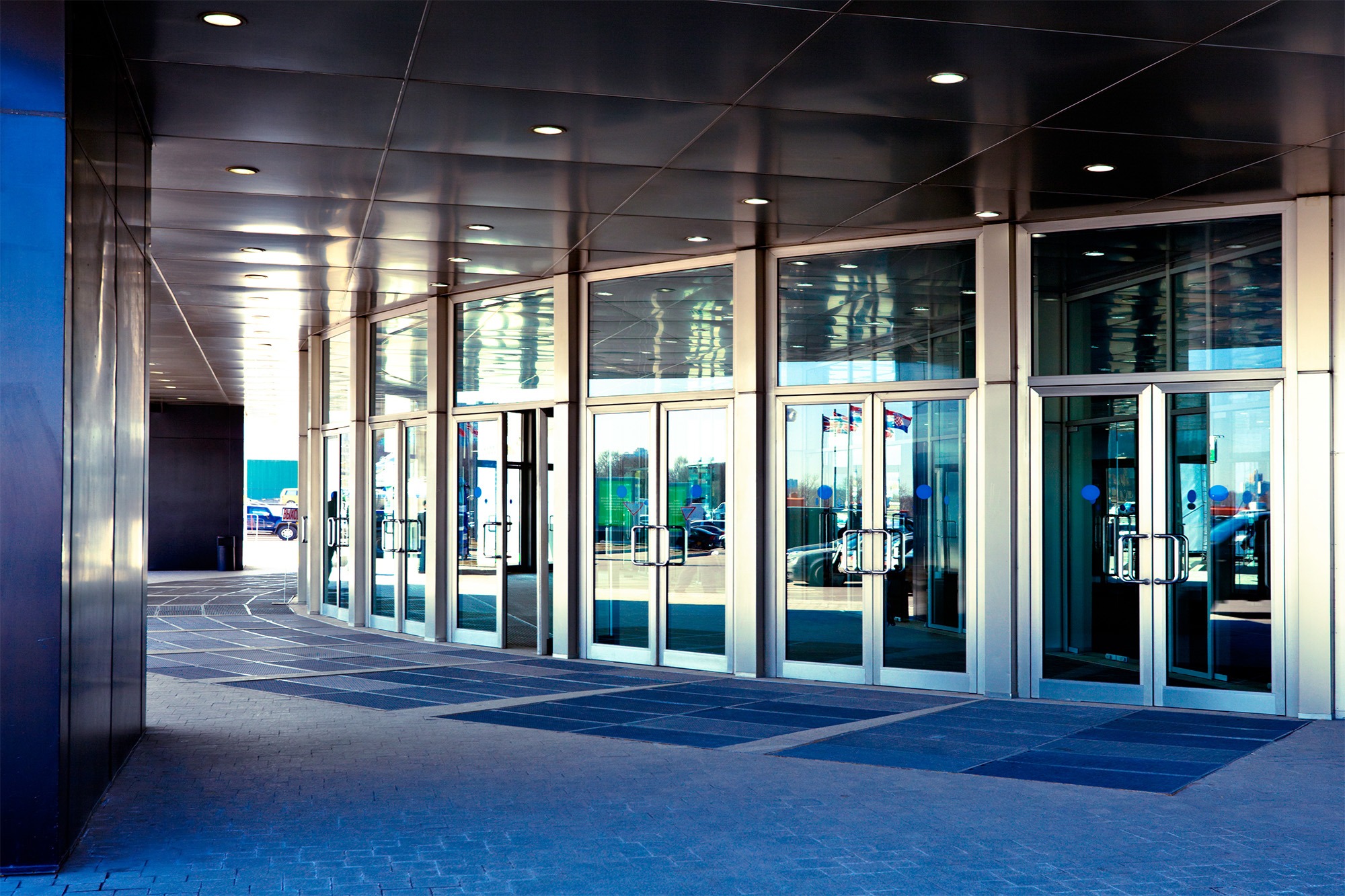Modern glass entrance of a building, showcasing curved doors and sleek architecture. The scene highlights accessibility and design.