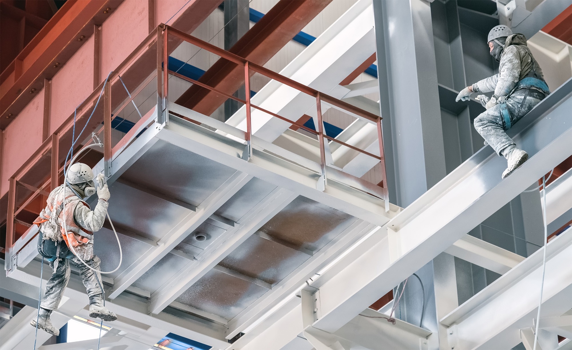 Two industrial climbers paint the metal frame of a power plant under construction